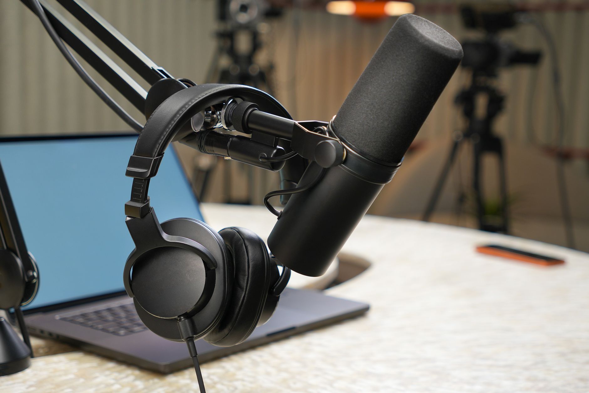 Headphones hanging on a podcast microphone over a laptop