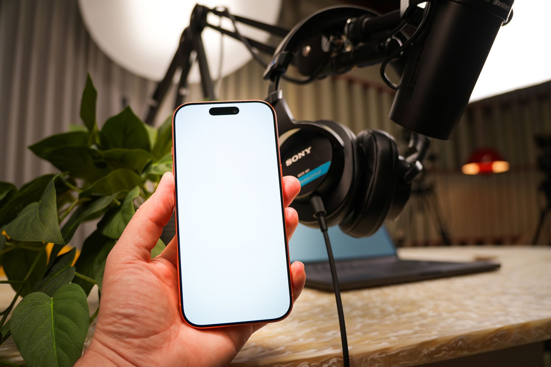 Hand holding a phone with a blank screen beside a podcast microphone